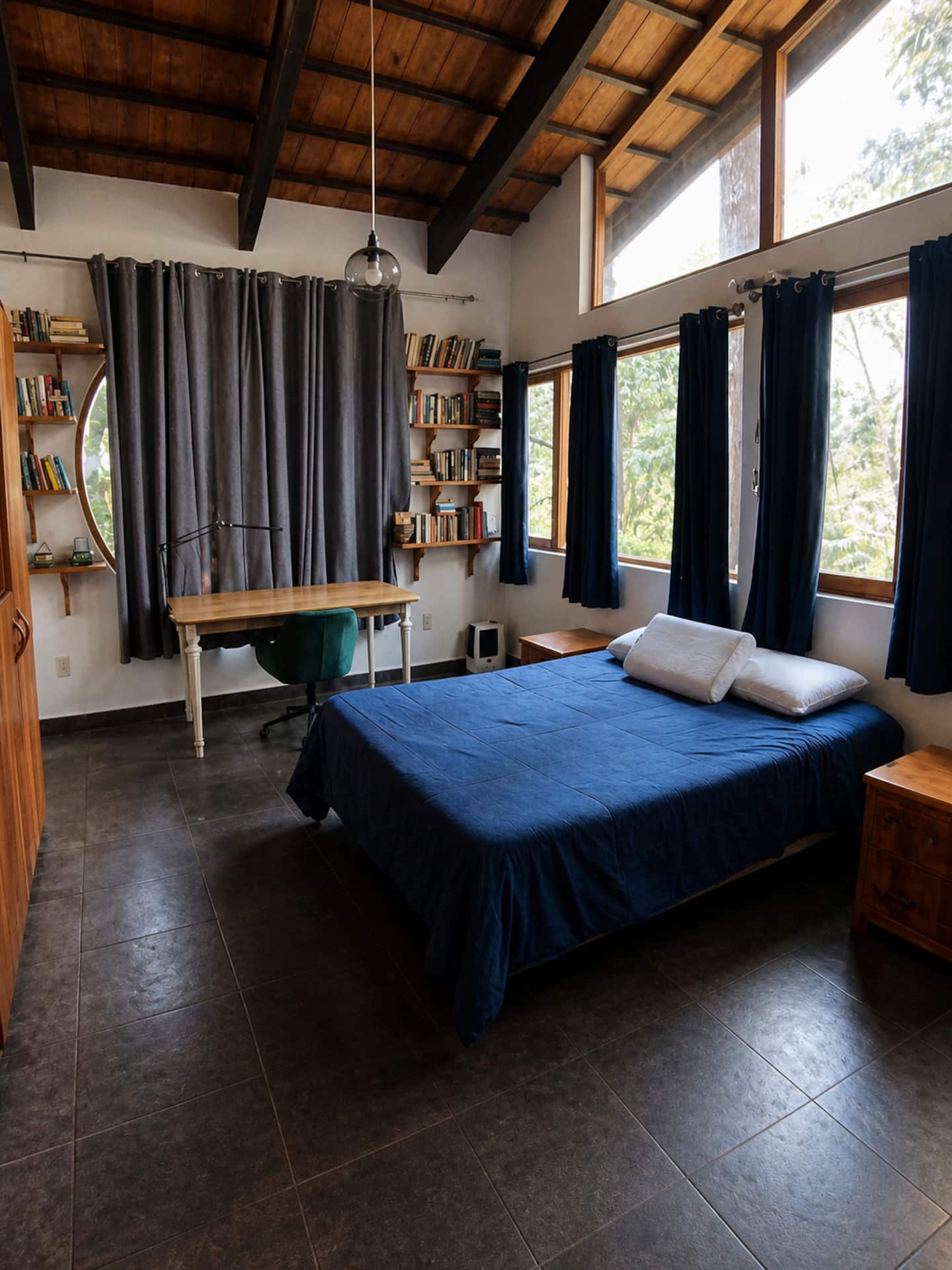 Habitación con ropa de cama azul, muebles de madera y ventanas al bosque